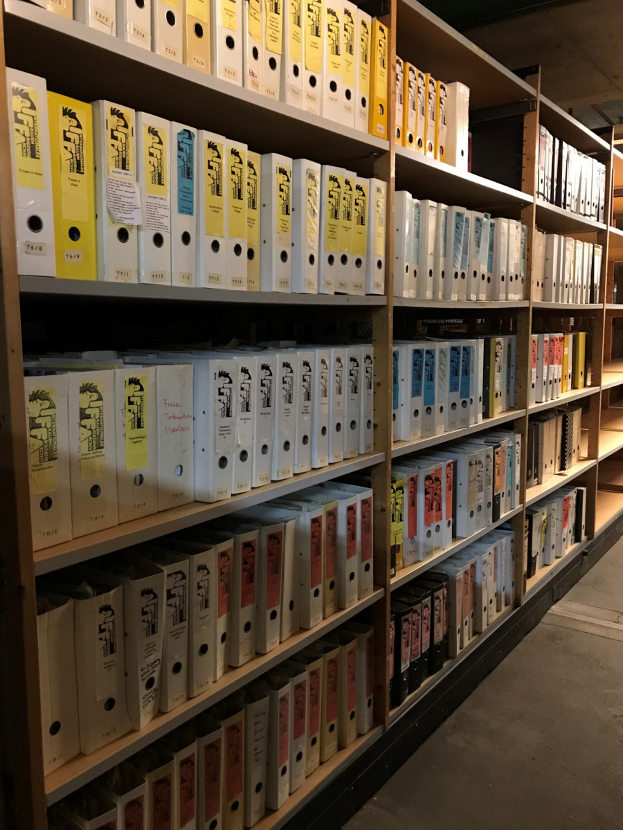 Blick auf Archivregale mit Aktenordnern. Auf den Ordnerrücken sind rote, blaue, weiße und gelbe Schilder, bedruckt mit dem IFFA-Logo, beklebt.