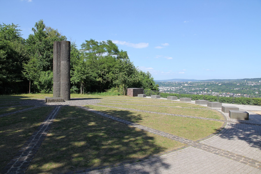 Zum anderen eine dreigliedrige Basaltstele, die im Zentrum eines Platzes in den Himmel ragt und von der ein gepflasterter Strahlenkranz ausgeht, dessen Zwischenflächen begrünt sind. Auch hier bildet die Weite des Ausblickes auf das Tal einen wesentlichen Bestandteil der Aufnahme.